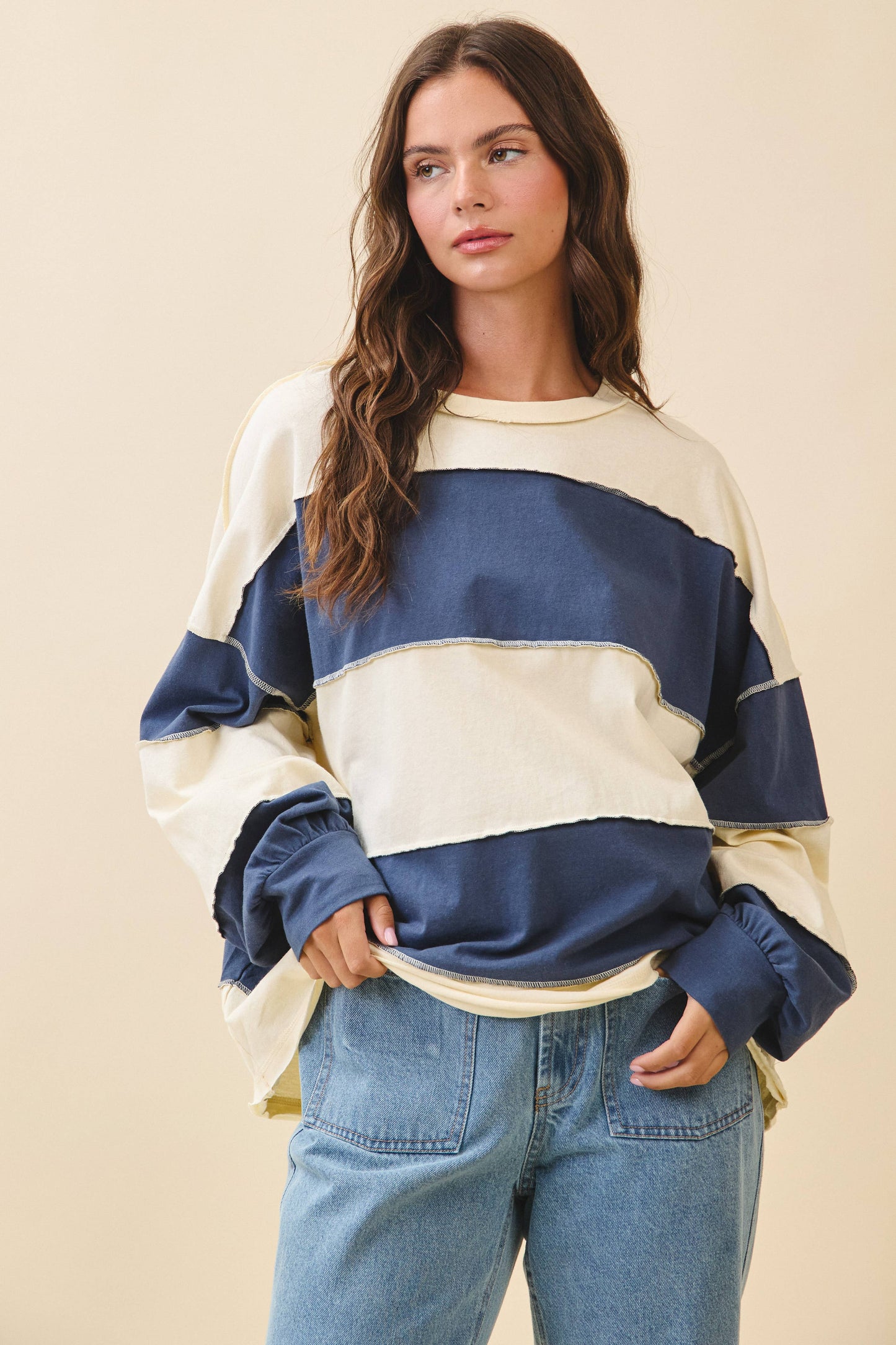 Woman wearing a blue and white striped sweater with blue jeans on a beige background
