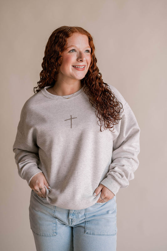 Woman wearing a light gray sweatshirt with a cross design on a beige background