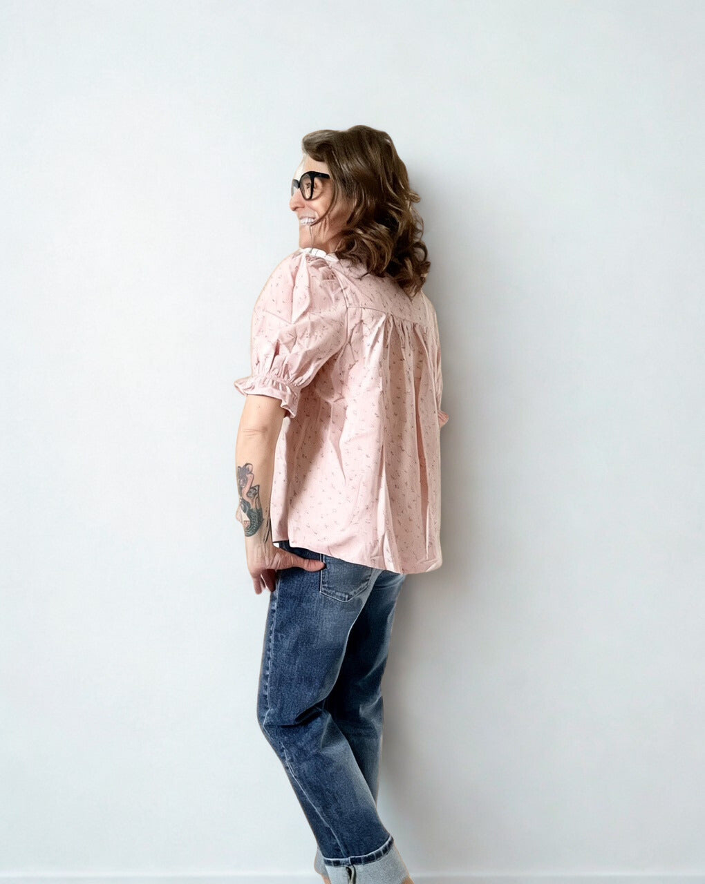 Person wearing a light pink blouse and blue jeans against a white wall
