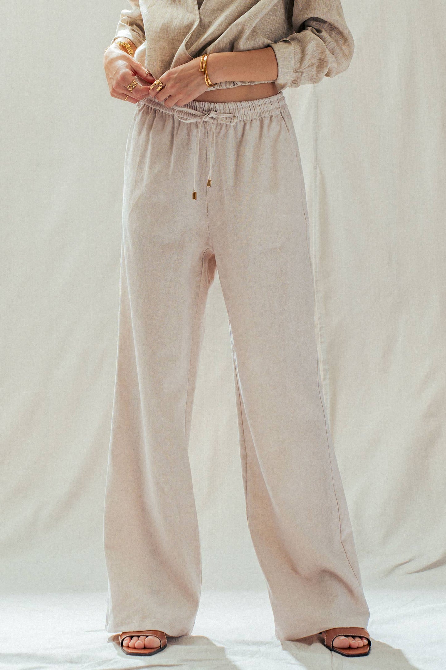 Person wearing beige pants and a matching top on a plain background