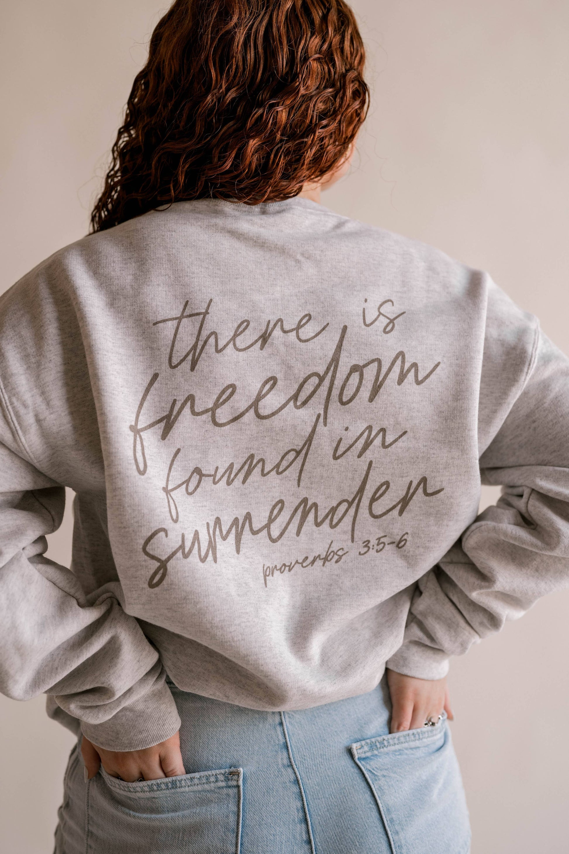 Person wearing a gray sweatshirt with text 'there is freedom found in surrender' on the back.