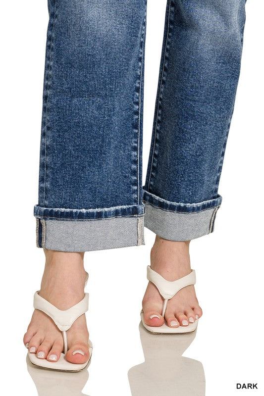 Close-up of rolled-up blue jeans and white sandals on a reflective surface.