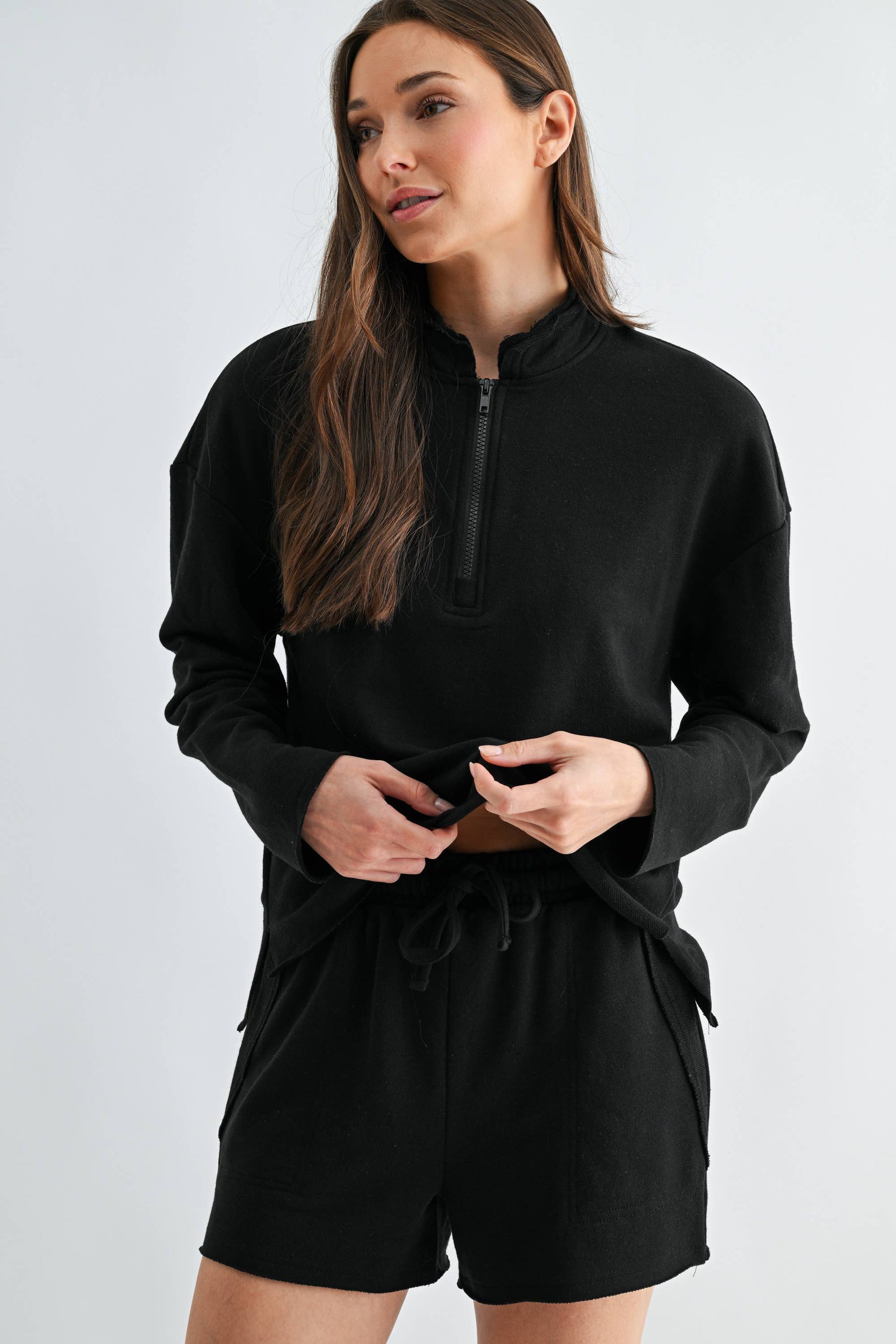 Woman wearing a black outfit with a high collar on a light gray background