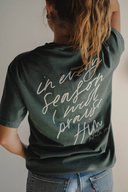 Person wearing a green t-shirt with text on the back, standing against a neutral background