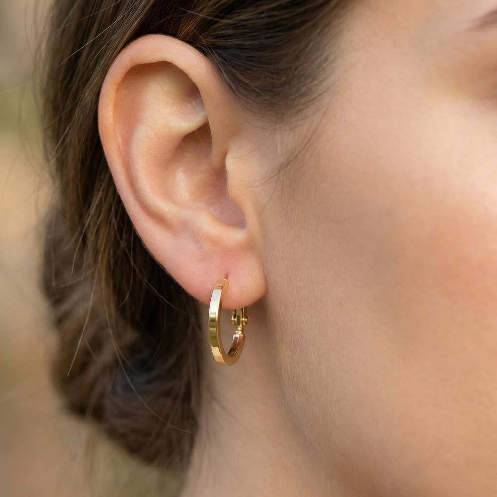 Close-up of an ear wearing a gold hoop earring with a blurred background