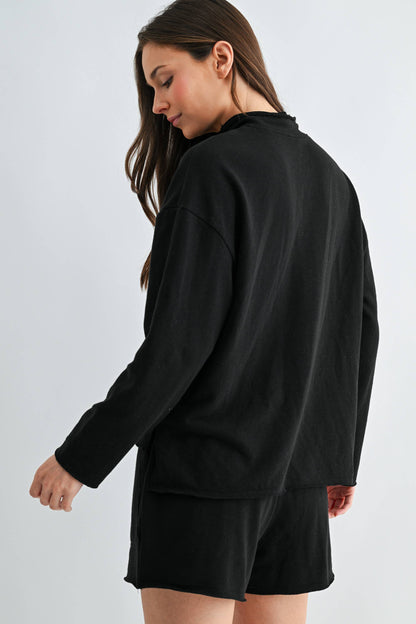 Woman wearing a black oversized sweatshirt and shorts on a light gray background