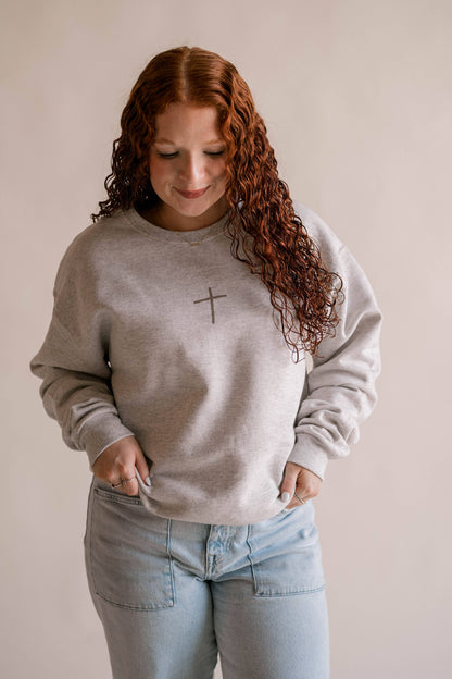 Woman wearing a gray sweatshirt with a cross design on a plain background