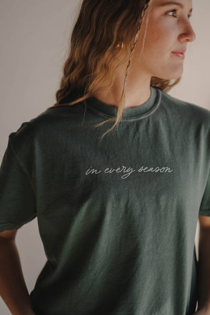 Person wearing a green t-shirt with 'in every season' text.