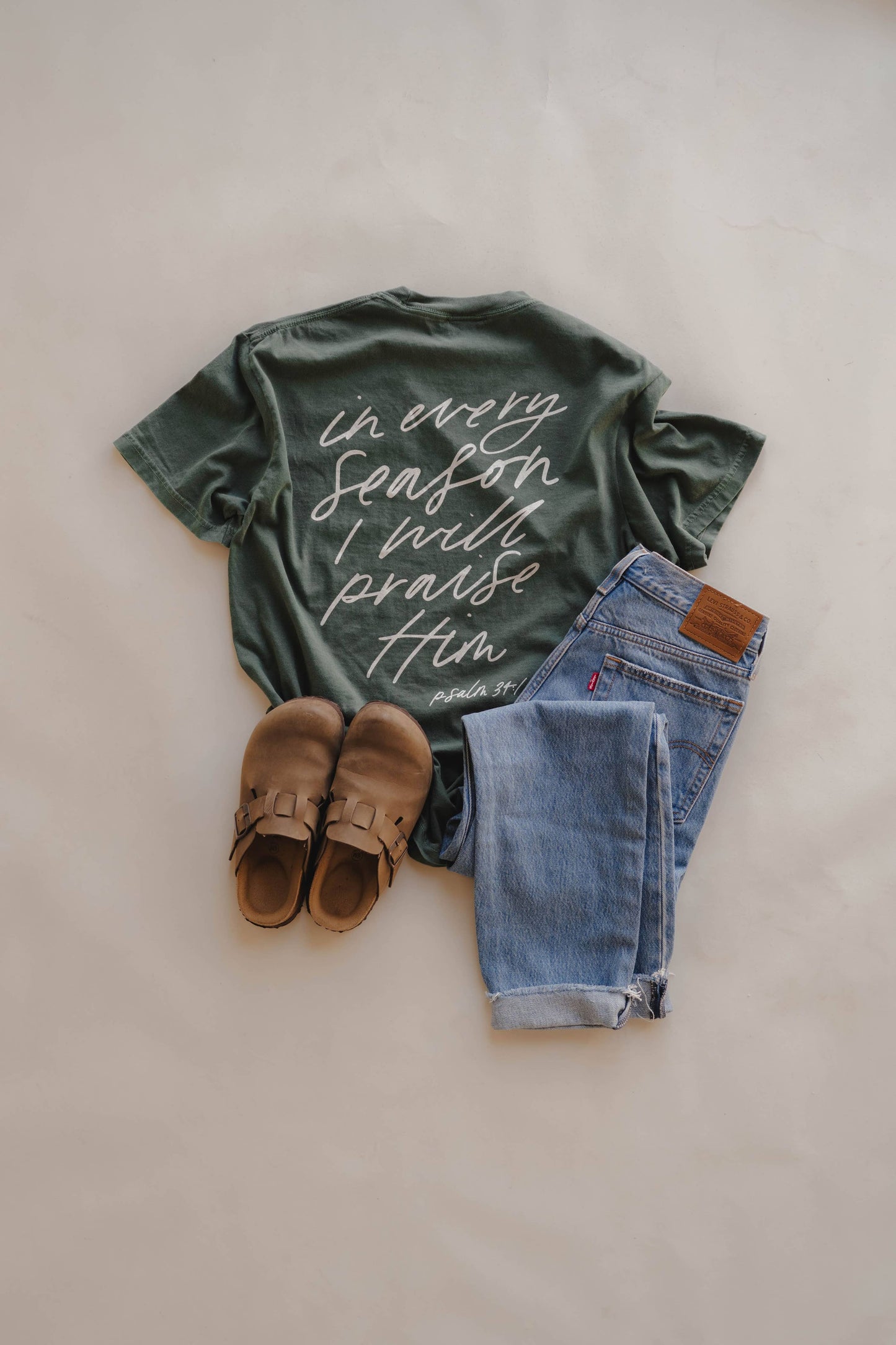 Green t-shirt with text, blue jeans, and brown shoes on a light background