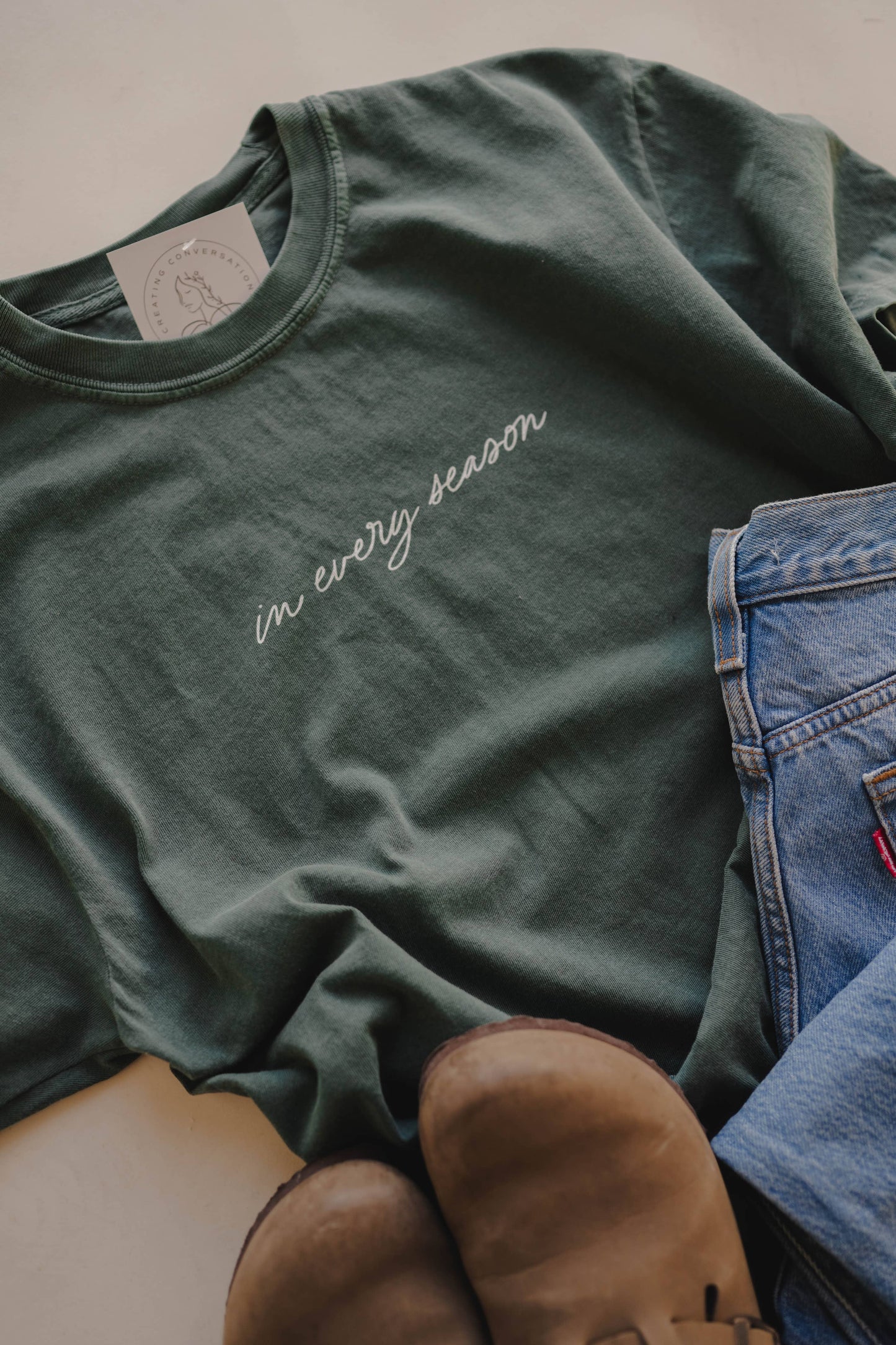 Green t-shirt with 'in every season' text on a neutral background