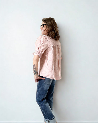 Person wearing a light pink blouse and blue jeans against a white wall