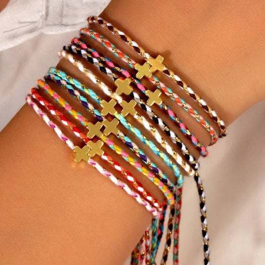 Multicolored braided bracelets with gold crosses on a wrist against a neutral background