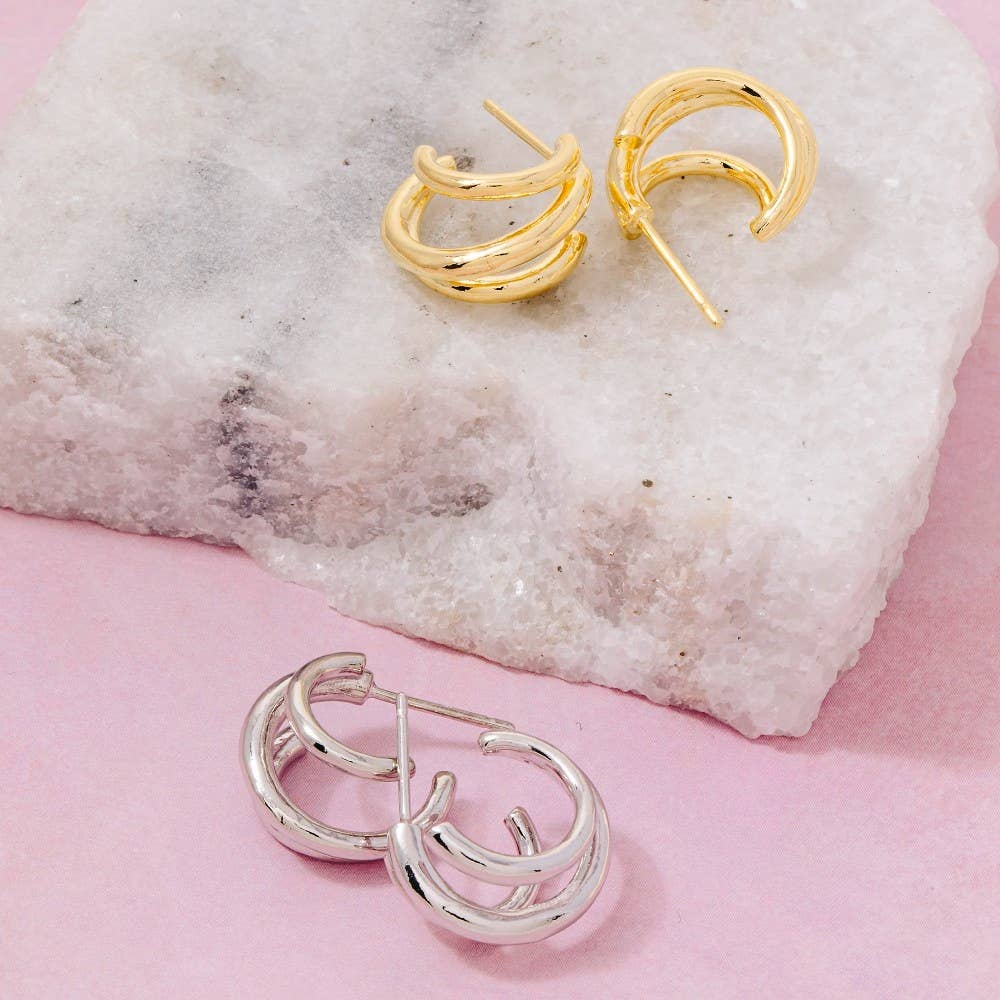 Gold and silver hoop earrings on a textured stone surface with a pink background