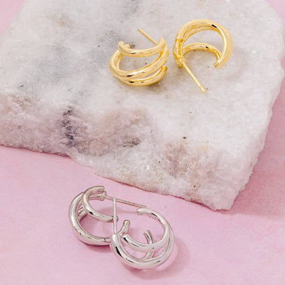 Gold and silver hoop earrings on a textured stone surface with a pink background