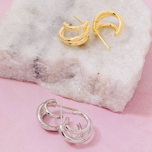 Gold and silver hoop earrings on a textured stone surface with a pink background