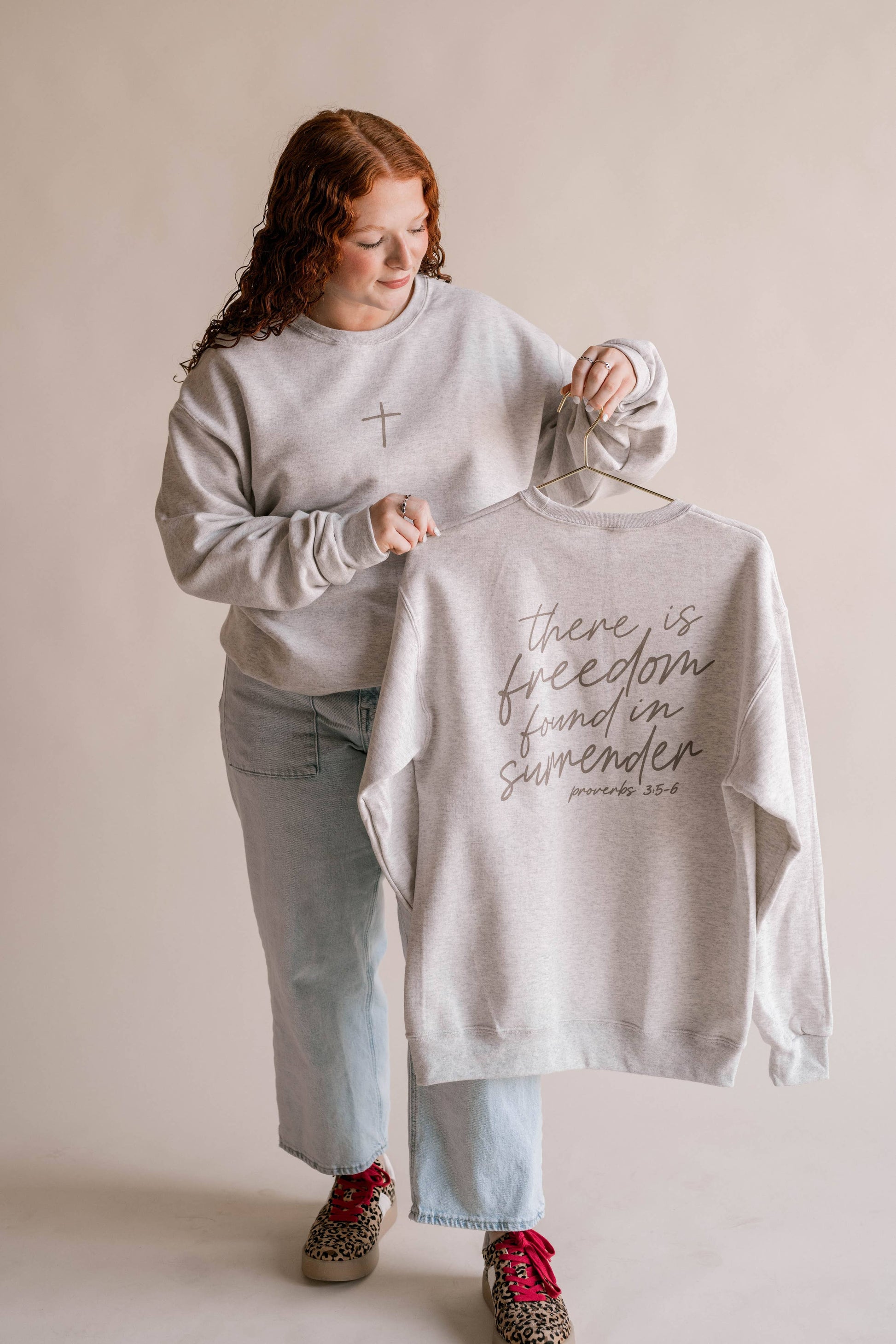 Person holding a t-shirt with text on a hanger against a plain background