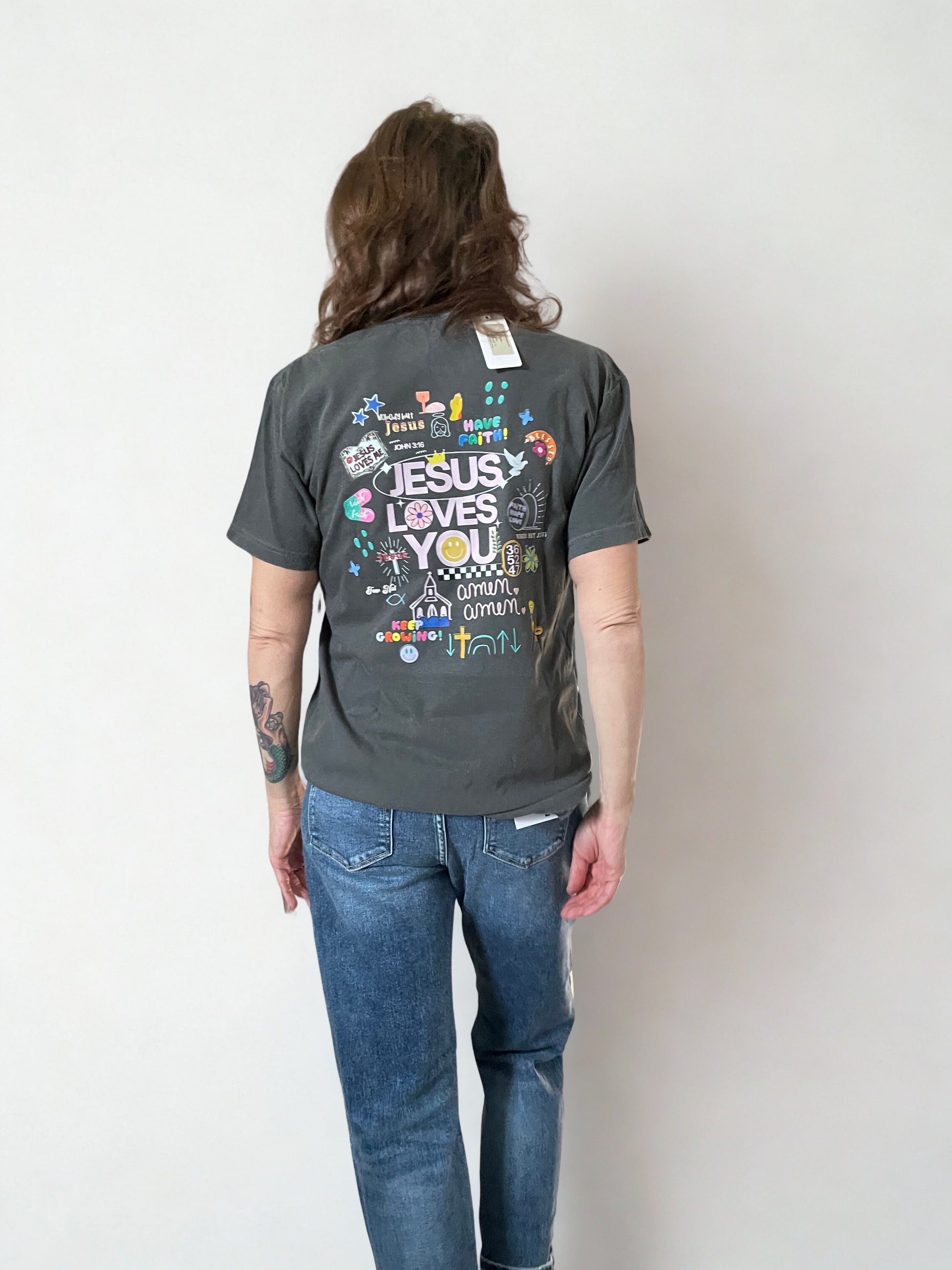 Person wearing a gray t-shirt with 'Jesus Loves You' text on the back, standing against a plain background.