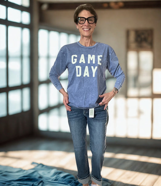 Woman wearing a blue 'GAME DAY' sweatshirt and jeans in a bright room.