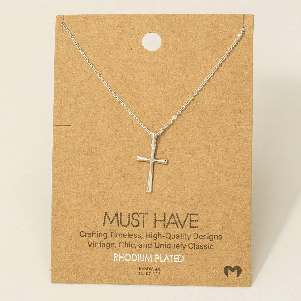 Silver cross necklace on a brown card with text about the brand.