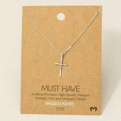 Silver cross necklace on a brown card with text about the brand.