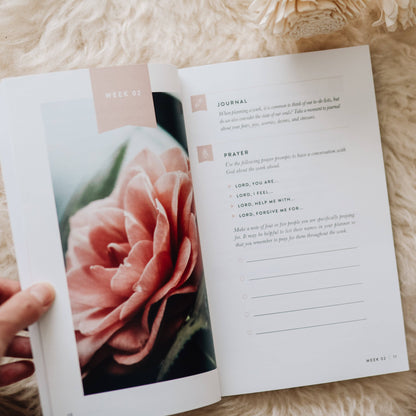 Open book with a pink rose on one page and text on the other, held by a hand on a textured surface.